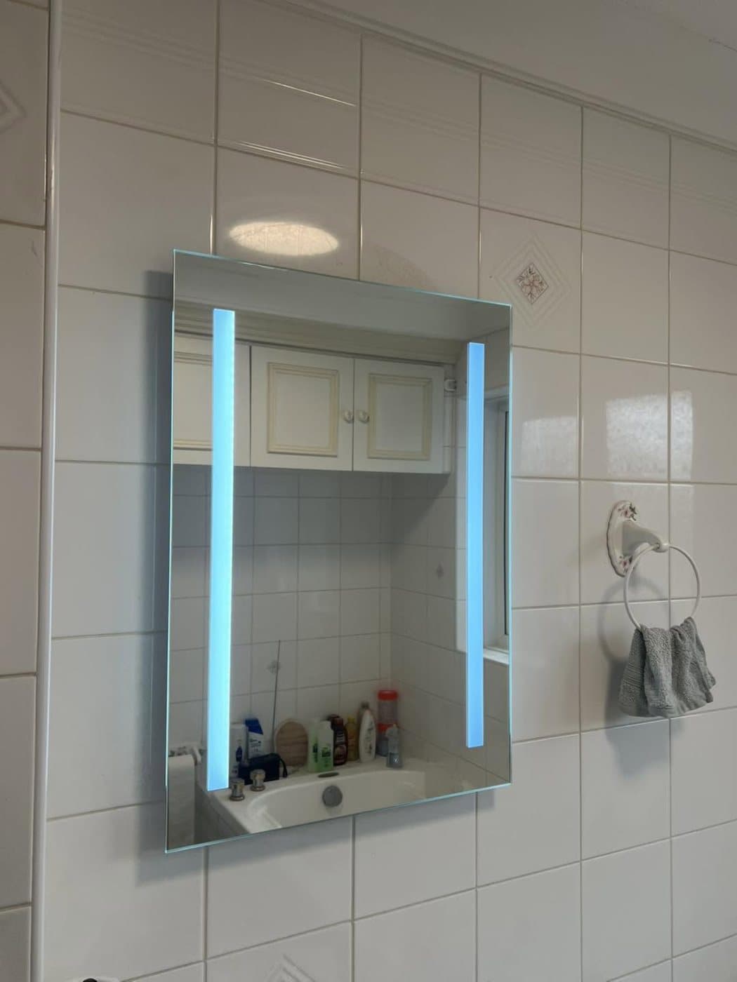 Backlit LED illuminated mirror cabinet fitted in a tiled bathroom