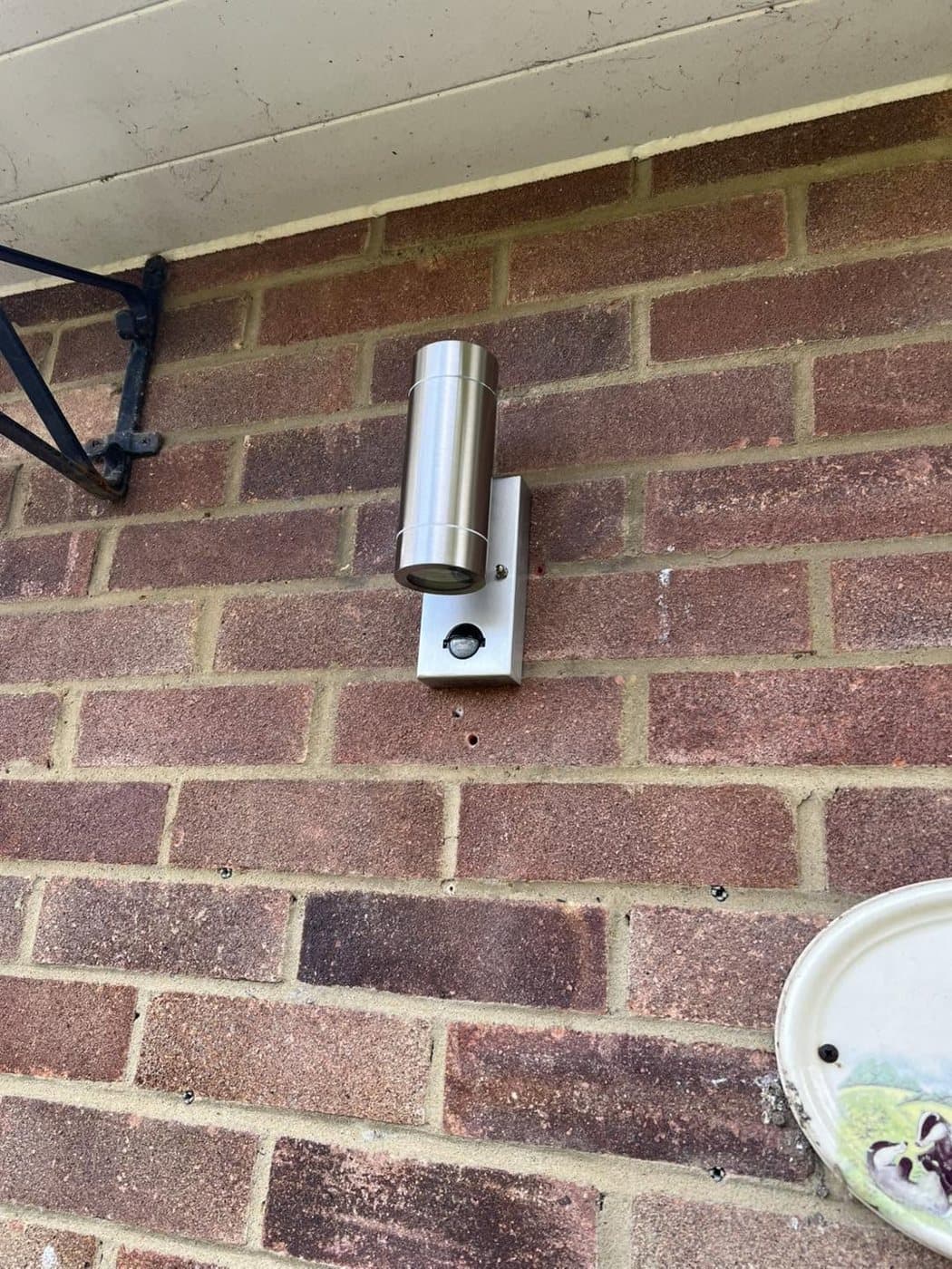 Brushed-steel bollard-style wall light fitted to an exterior brick wall