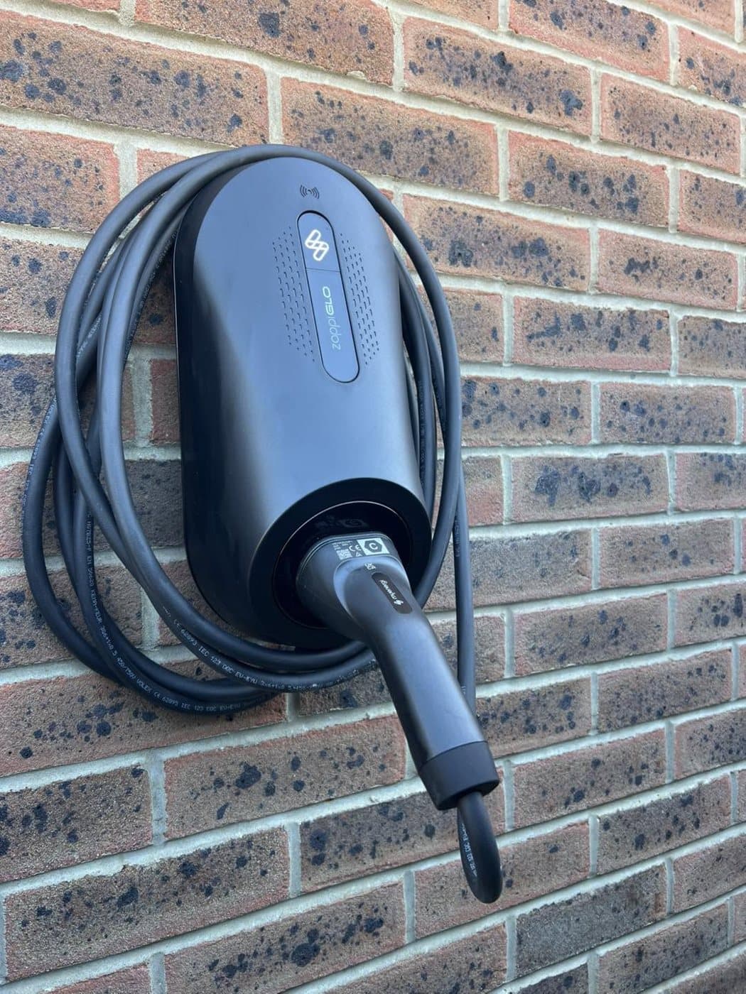 Tethered home EV charger fitted on a brick wall with the cable neatly coiled