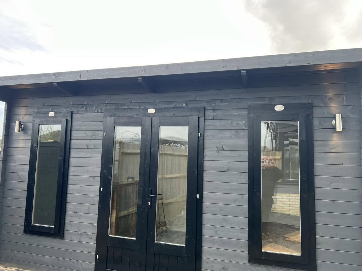 Dark-clad garden room with exterior wall lights either side of the doors