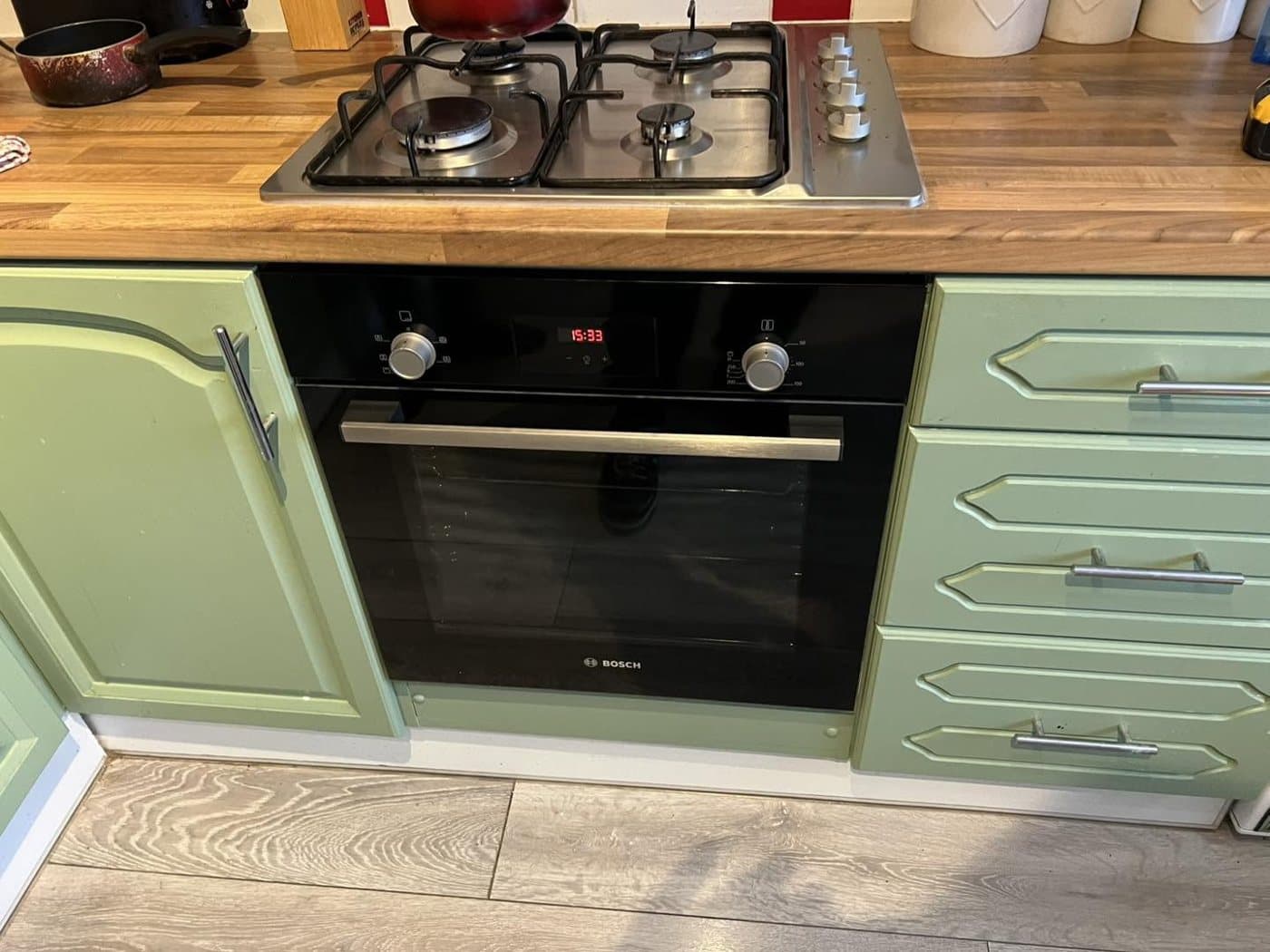Sage-green fitted kitchen with a gas hob, integrated oven and under-unit power