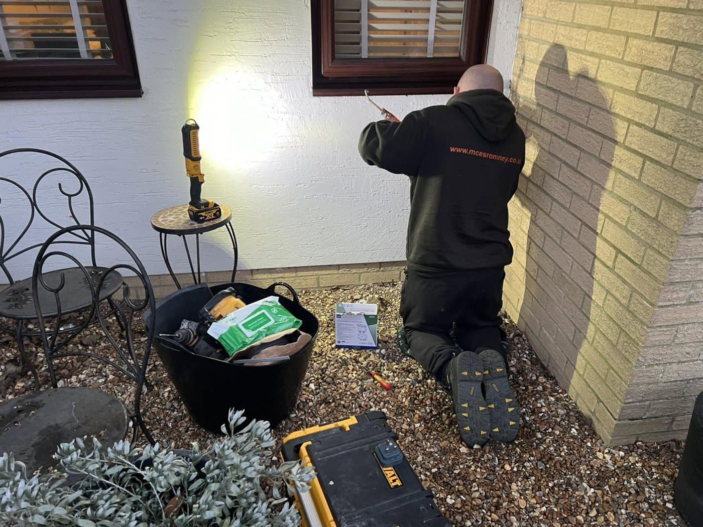 Outdoor wall lantern being fitted at dusk, lit against the brickwork